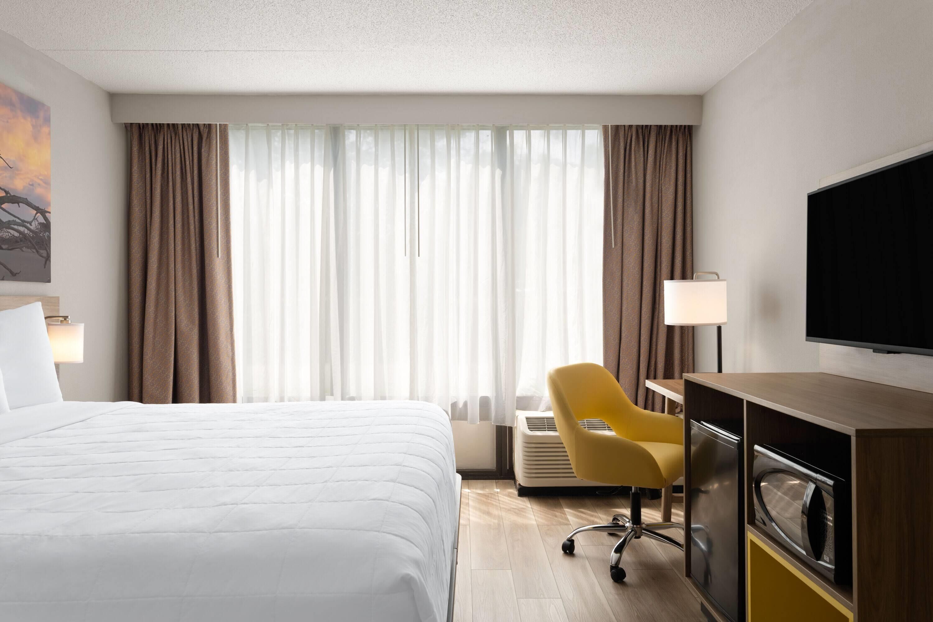 A hotel room with a bed, a desk, a chair, a TV, and a window with curtains.