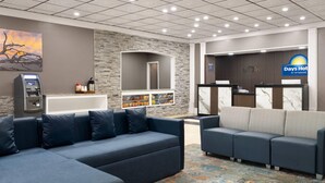 Un vestíbulo de hotel con mostrador de recepción, zona de estar con sofás, quiosco de autoservicio y una pared decorativa de piedra.
