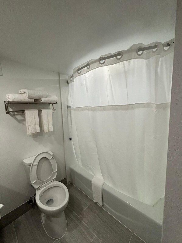 A bathroom with a toilet, a towel rack with towels, and a shower curtain.