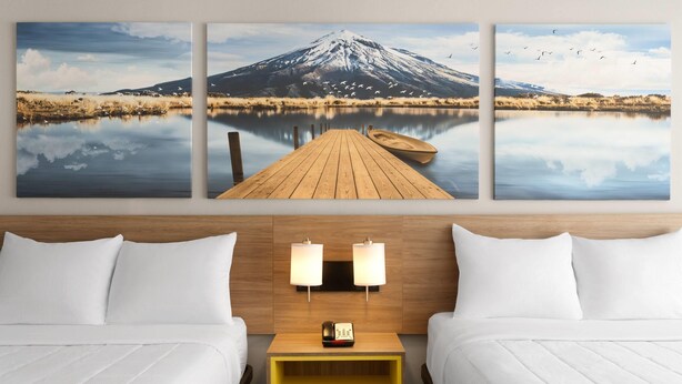 Una habitación de hotel con dos camas, una mesita de noche de madera y una lámpara fijada a la pared.