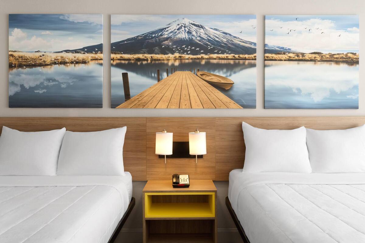 A hotel room with two beds, a wooden nightstand, and a wall-mounted lamp.