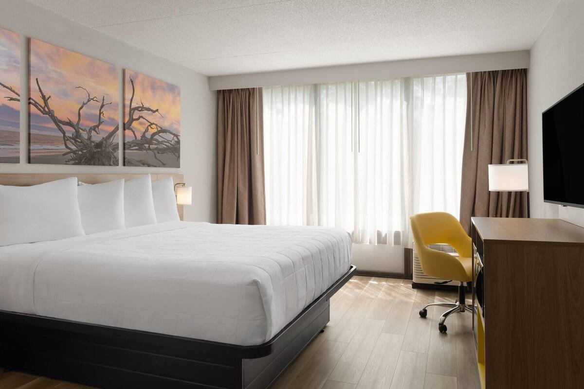 A hotel room with a large bed, a desk, a chair, and a TV.
