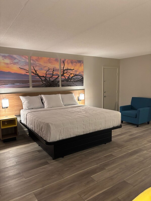 Un dormitorio moderno con una cama grande, una mesita de noche, un sillón azul y decoración mural con motivos del atardecer.
