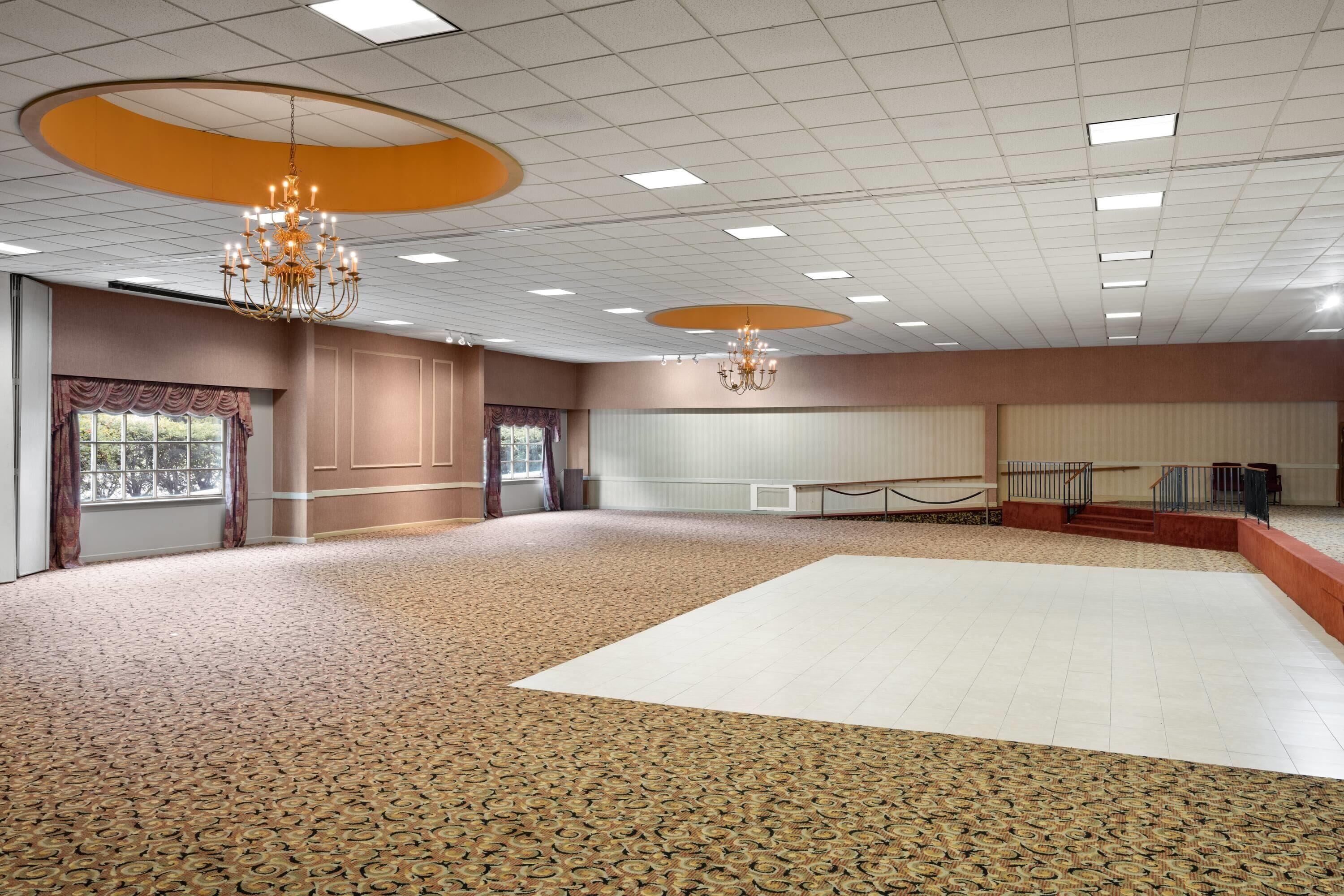 A spacious room with patterned carpet, a large white dance floor, and two chandeliers.