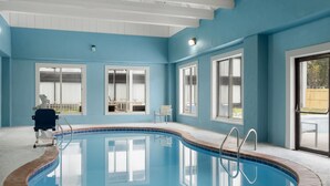 Una piscina interior con agua azul cristalina, rodeada de paredes blancas y amplios ventanales.