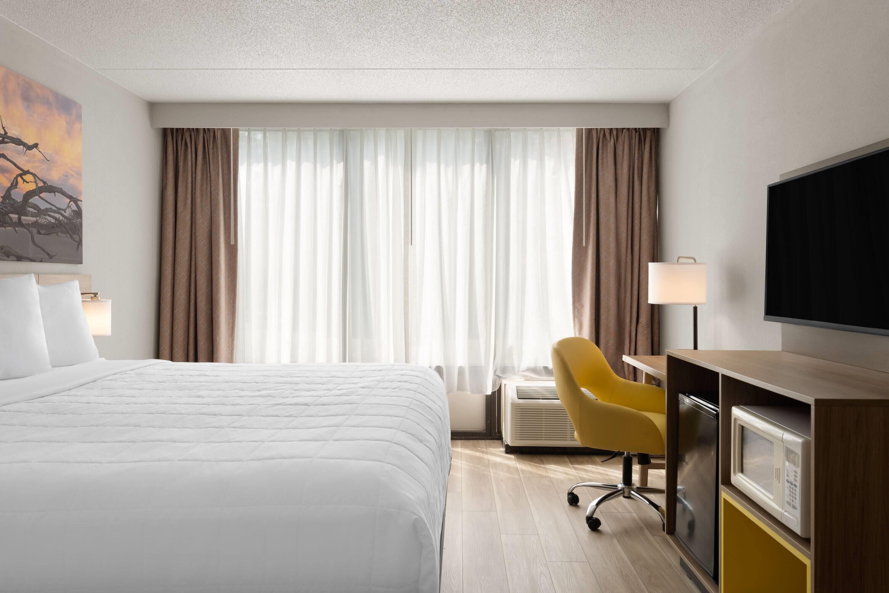 Habitación de hotel con cama, escritorio con silla, televisor y ventana con cortinas.