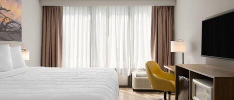 Habitación de hotel con cama, escritorio con silla, televisor y ventana con cortinas.