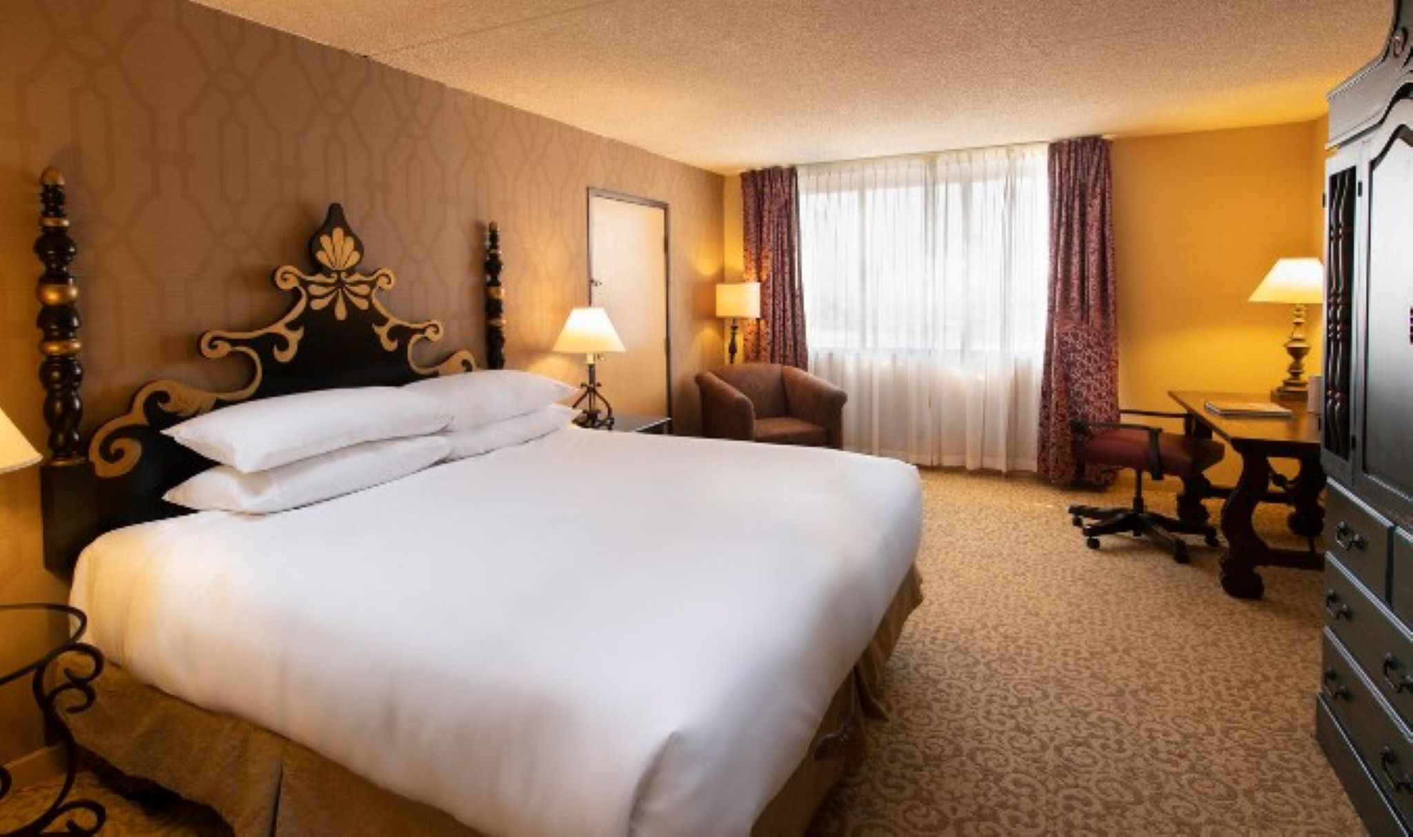 A hotel room with a large bed, a desk, a chair, a TV, and a window with curtains.