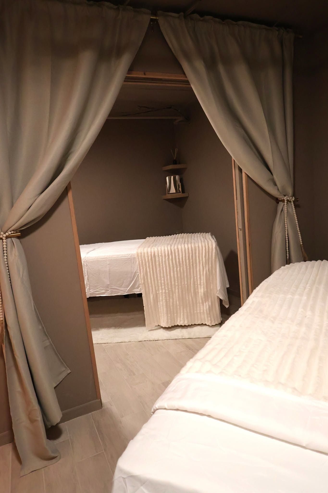 A room with two beds, a shelf with a container, and a hanging branch.