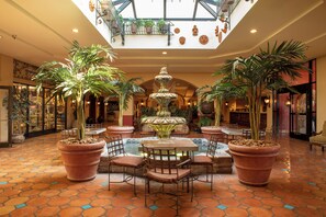 A spacious lobby with a central fountain, potted plants, and a high ceiling with skylights. - Hotel Encanto de Las Cruces (Las Cruces)