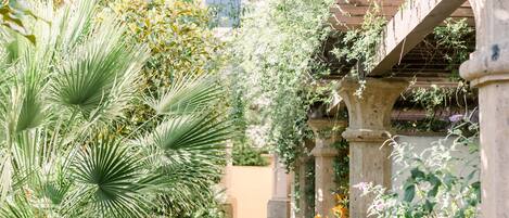A brick pathway lined with lush greenery and stone columns, leading to a covered area with a pergola.