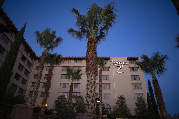 A hotel building with multiple floors, palm trees in front, and a clear sky.