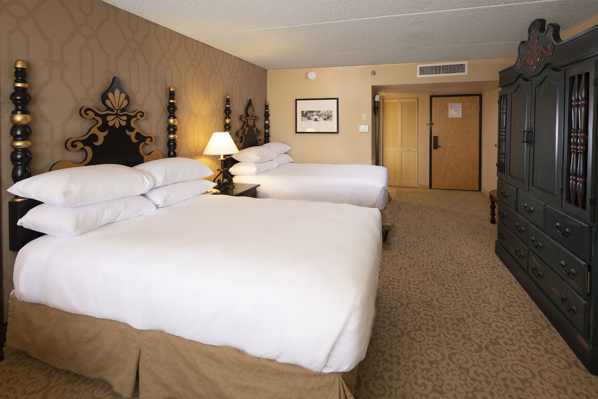 A hotel room with two beds, a dresser, a lamp, and a framed picture on the wall.