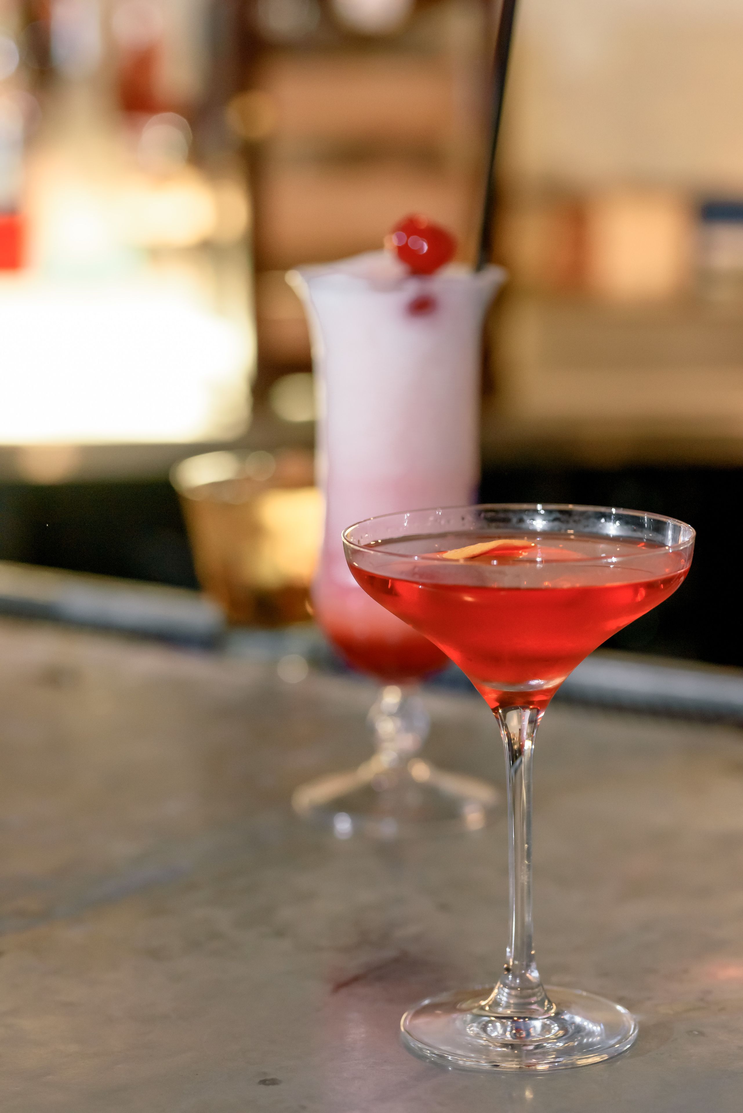 A martini glass with a red drink on a bar counter.