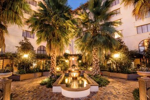 Un patio central con una fuente, rodeado de palmeras e iluminado con una luz ambiental.