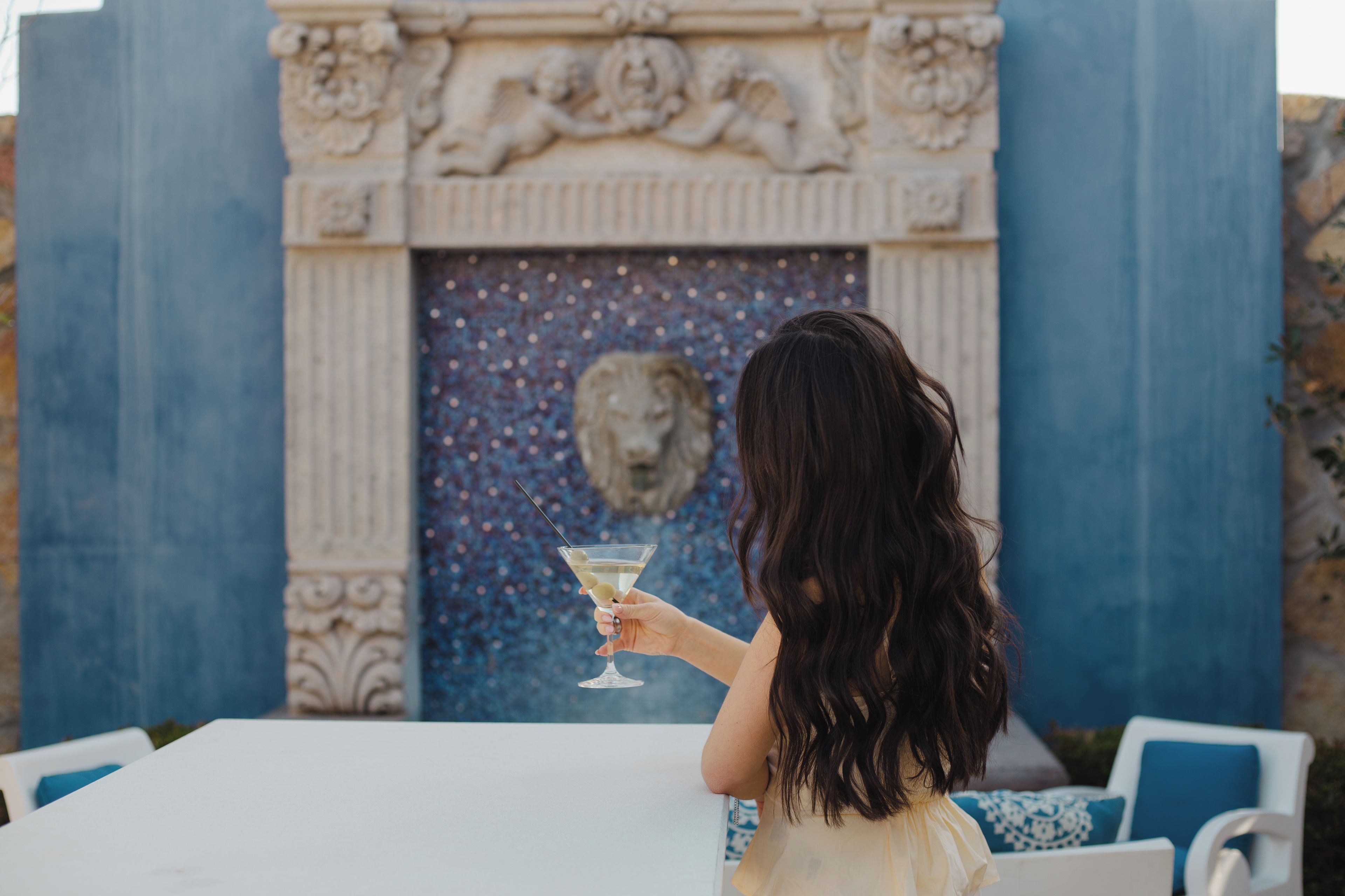 Eine Person hält ein Martini-Glas an einem Tisch mit dekorativem Hintergrund.