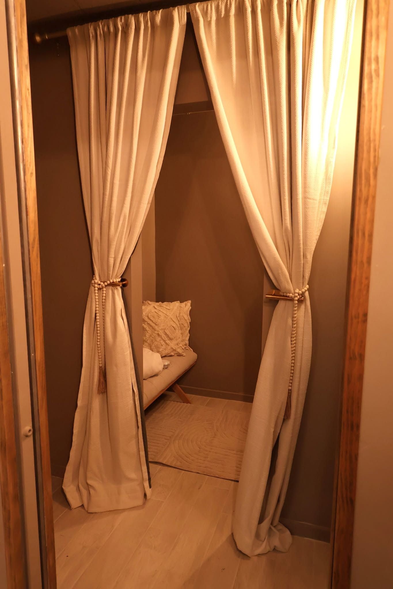 Una habitación con una cama, un tapete pequeño y cortinas atadas para dejar ver una zona de descanso.