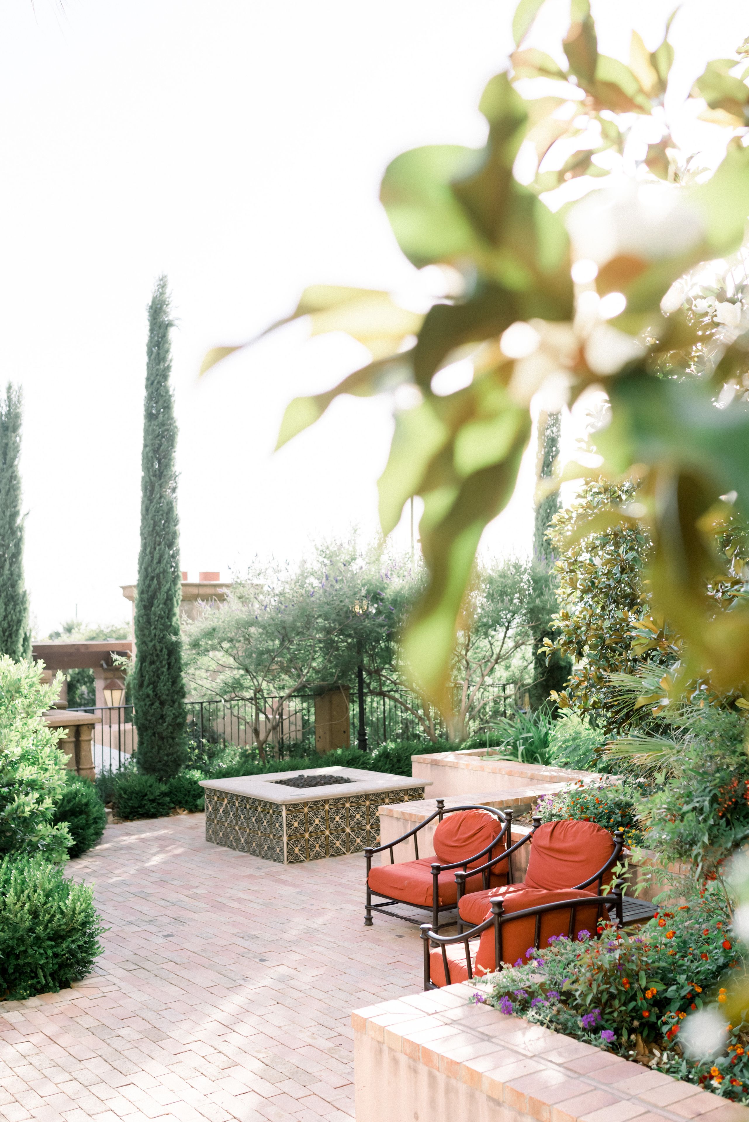 A patio with a fire pit, seating area, and lush greenery.