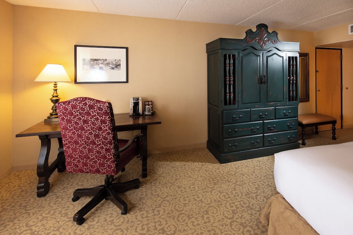 A hotel room with a bed, a desk with a chair, a dresser, a lamp, and a framed picture on the wall.