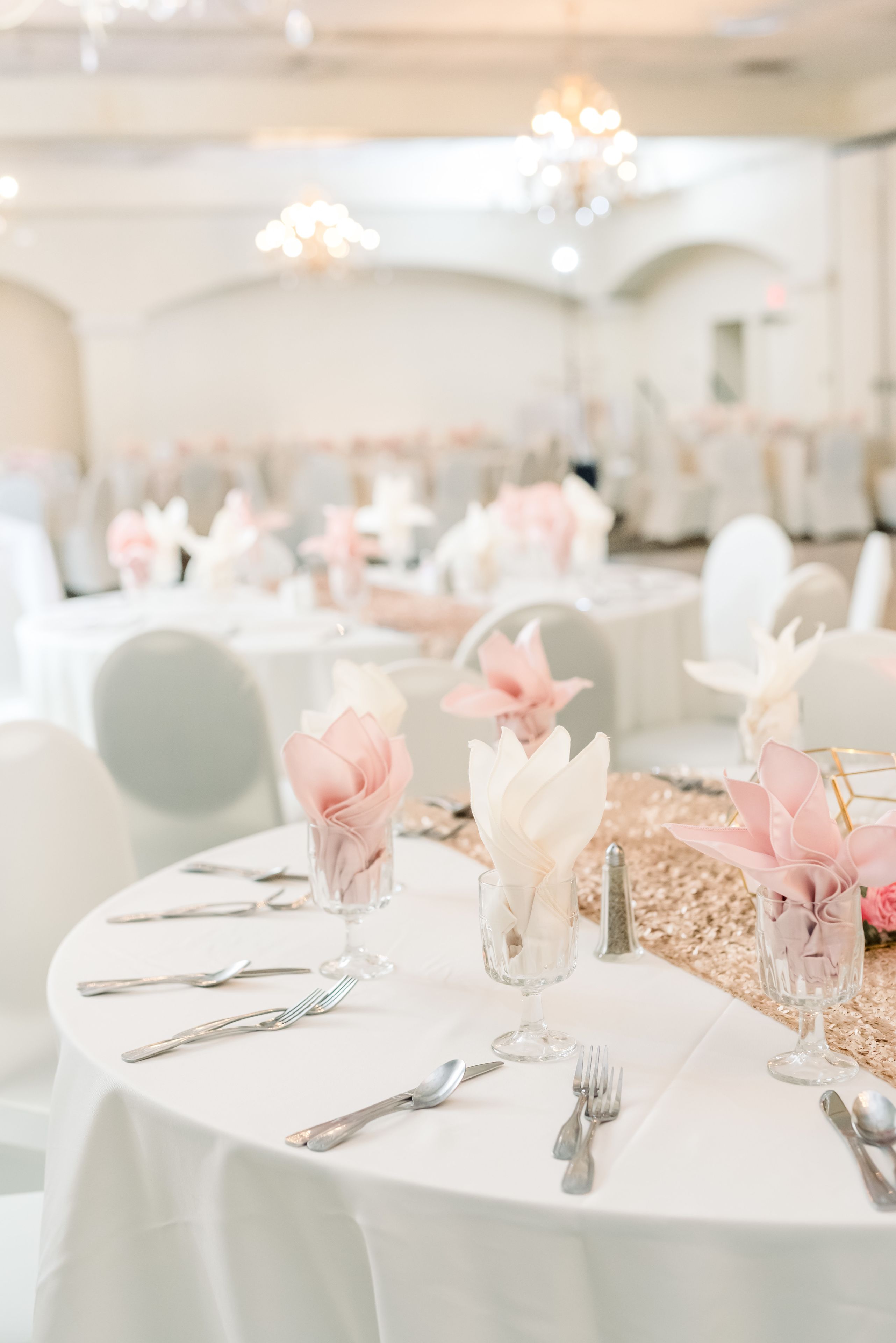 A banquet table set with white tablecloths, silverware, and pink and white floral centerpieces.