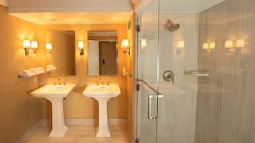 Une salle de bain avec deux lavabos, une douche en verre et des luminaires fixés au mur.