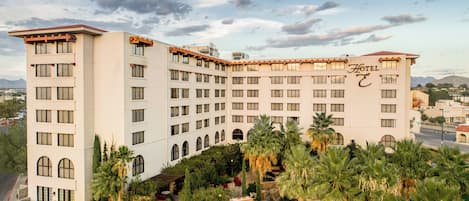 Et hotel med flere etager, en pool, palmer og et bjergrigt landskab i baggrunden.