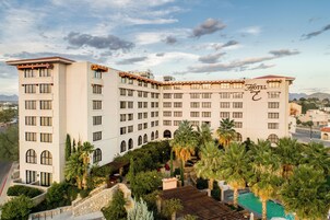Un hotel de varios pisos con piscina, rodeado de palmeras y un telón de fondo montañoso.