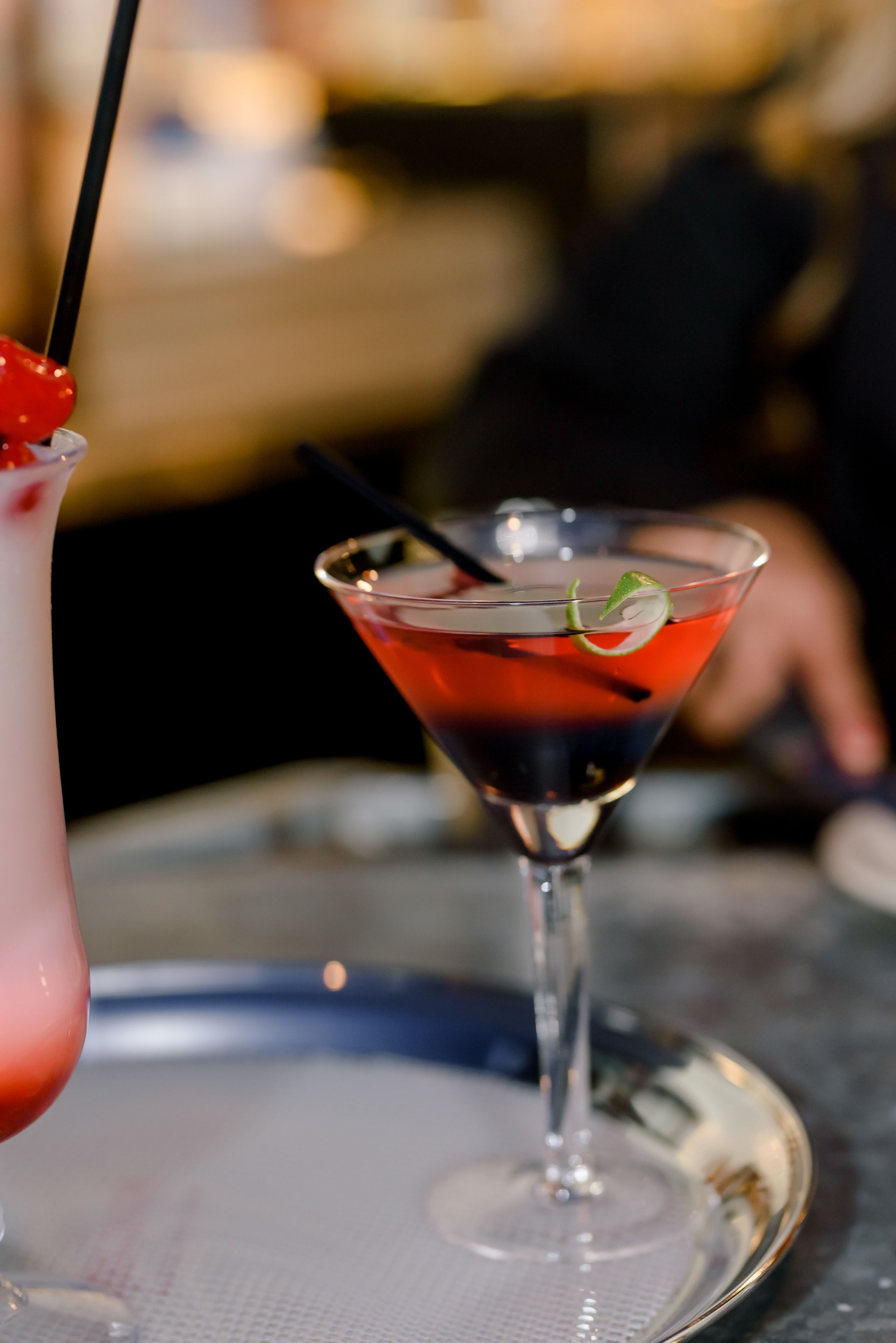 A martini glass with a red liquid and a lime garnish on a silver tray.