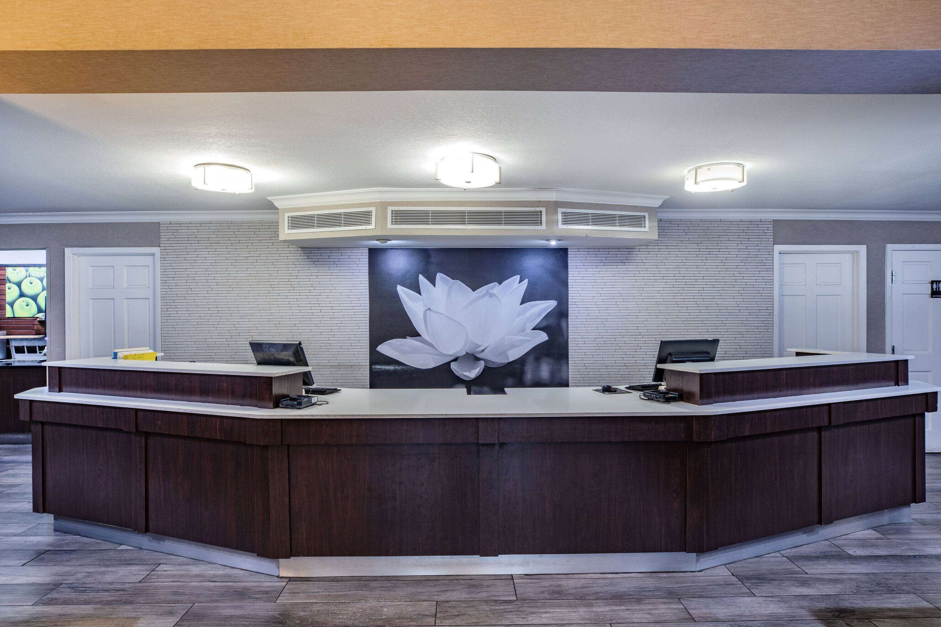 A reception desk with a large floral artwork above it, a white brick wall, and a ceiling with recessed lighting.