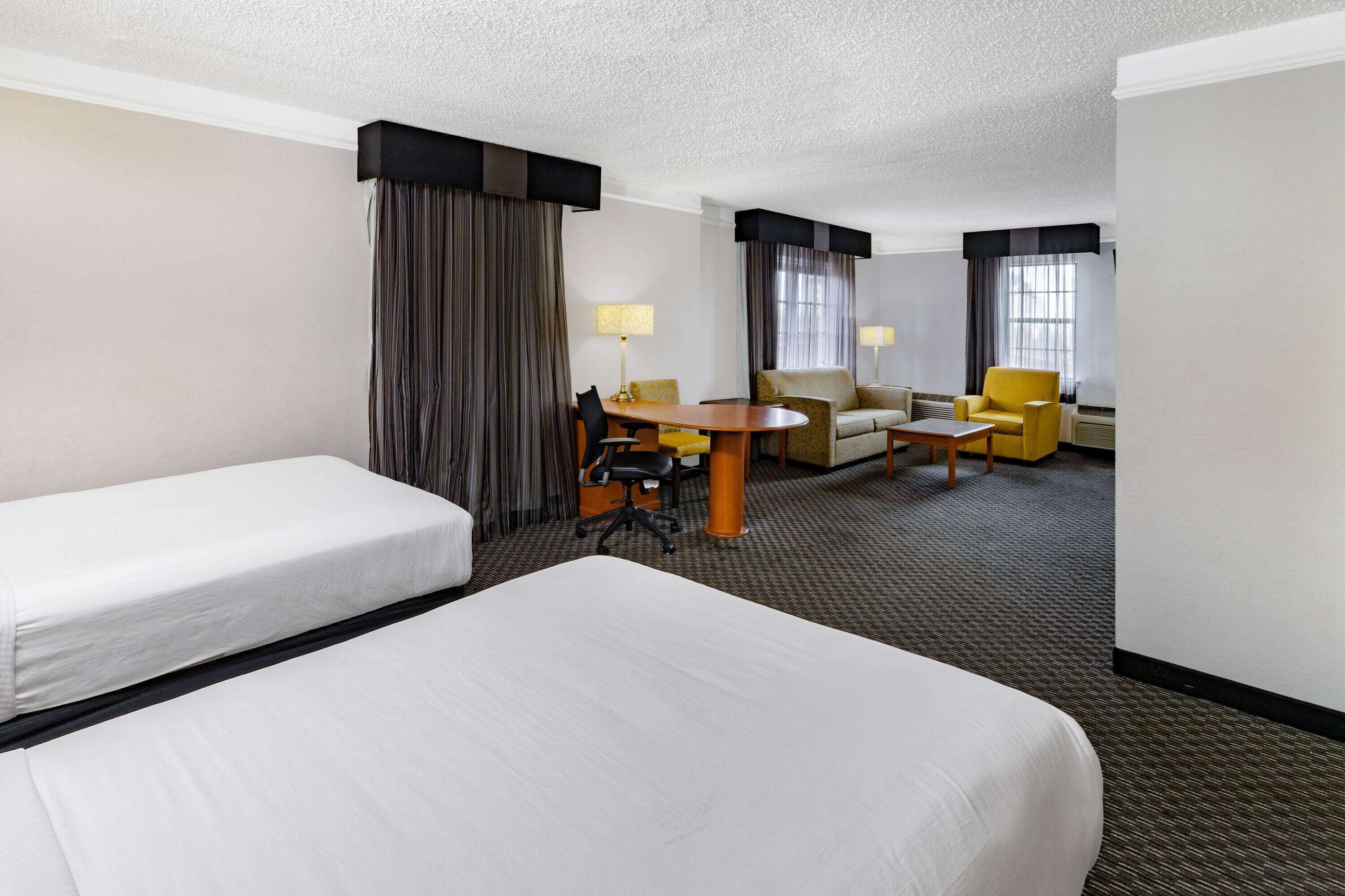 A hotel room with two single beds, a sofa, a small table, and a chair.