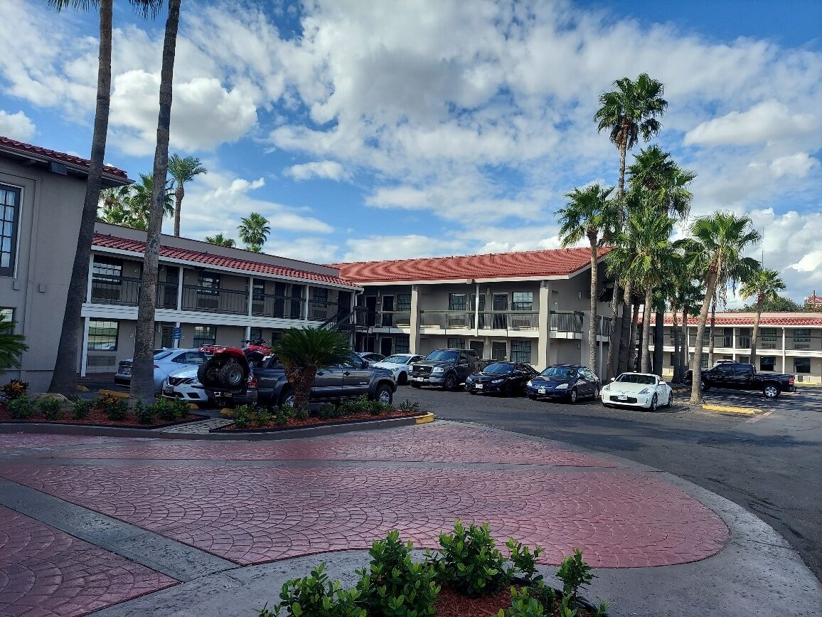Un hotel con estacionamiento, palmeras y cielo despejado.