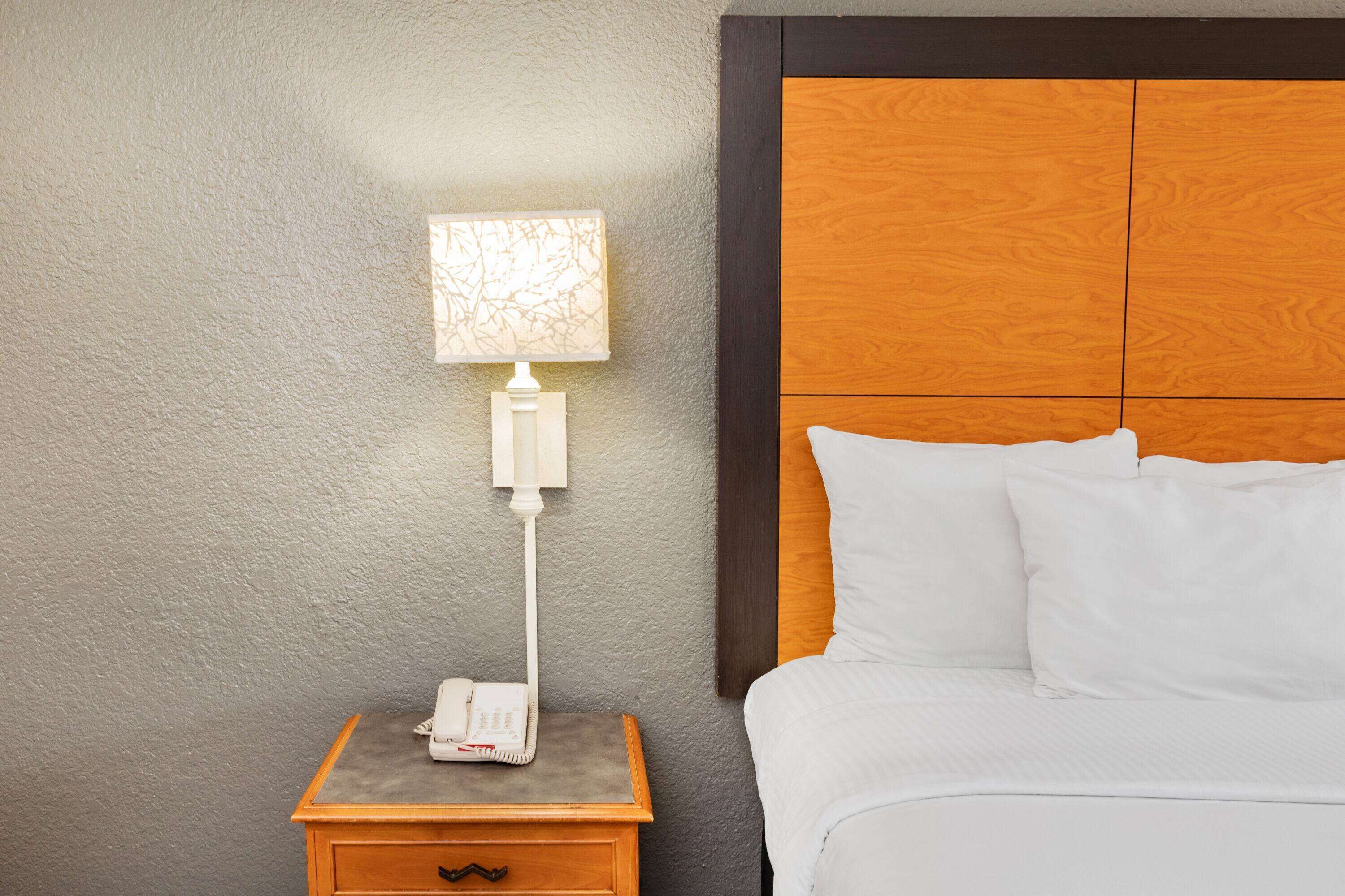 A hotel room with a wooden headboard, a bedside table with a lamp, and a telephone.