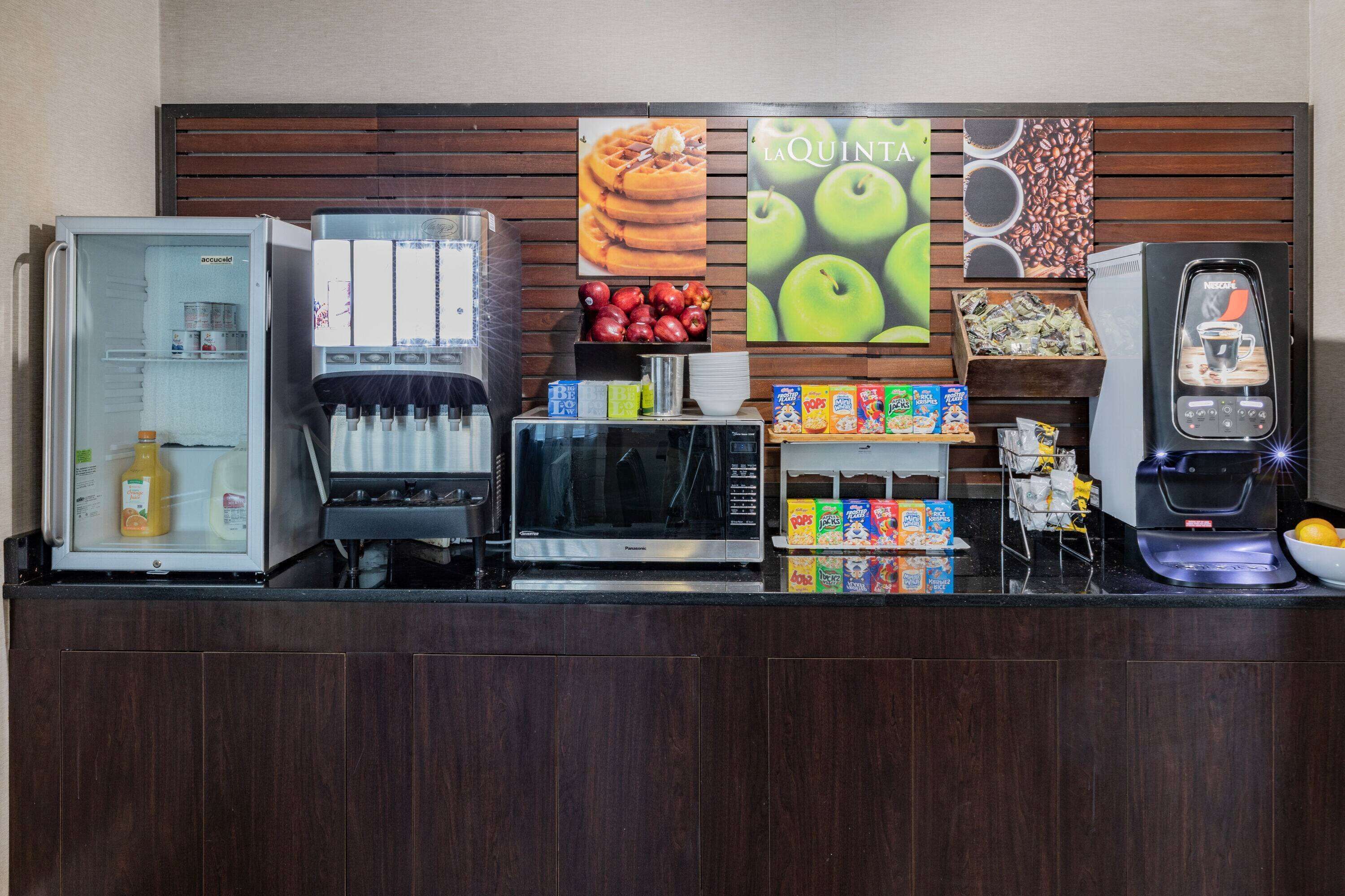 A self-service breakfast station with a refrigerator, microwave, and coffee machine.