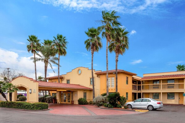 A hotel with a yellow facade, palm trees, and a red-tiled roof.