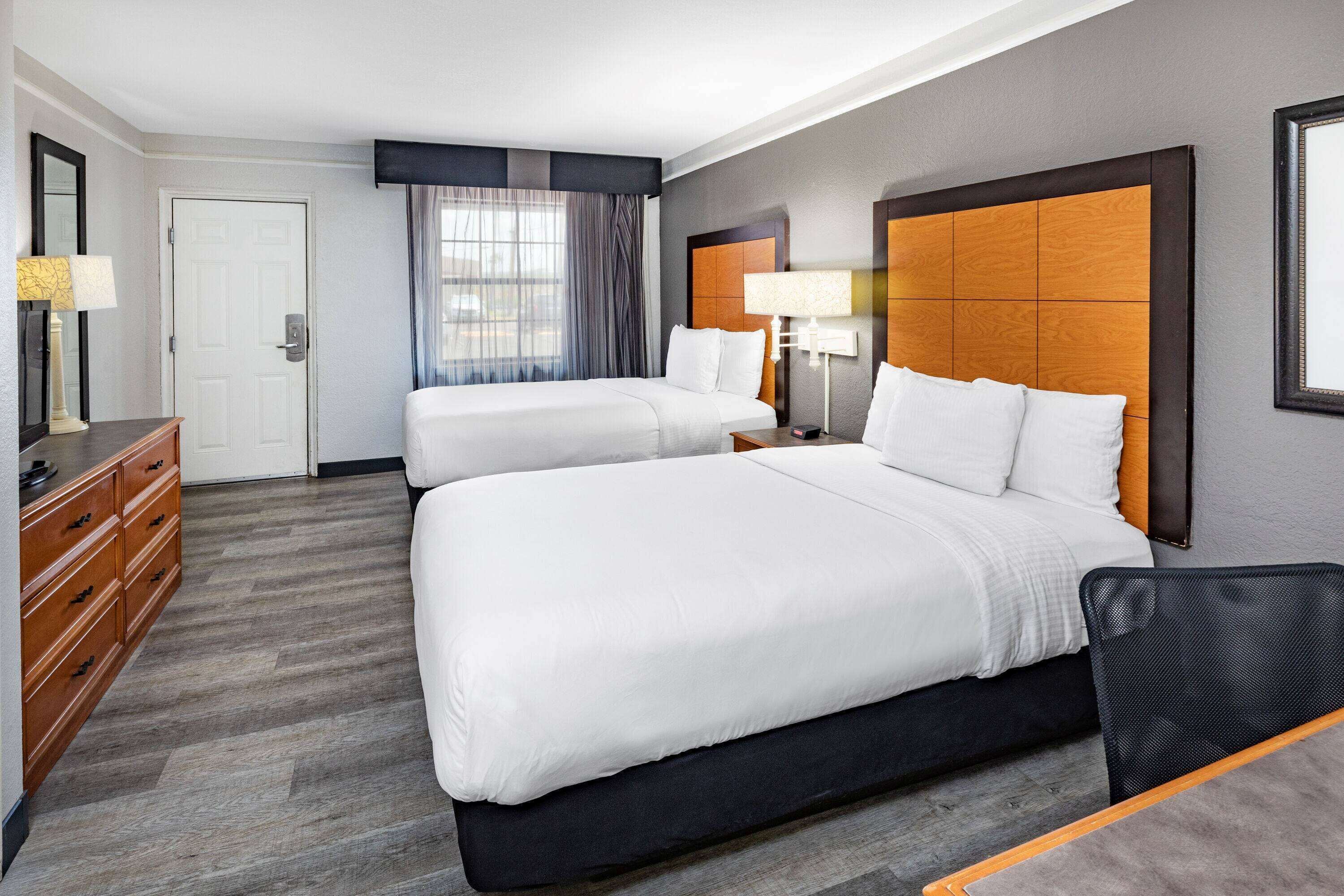 Une chambre d’hôtel avec deux lits, une commode et une fenêtre avec des rideaux.