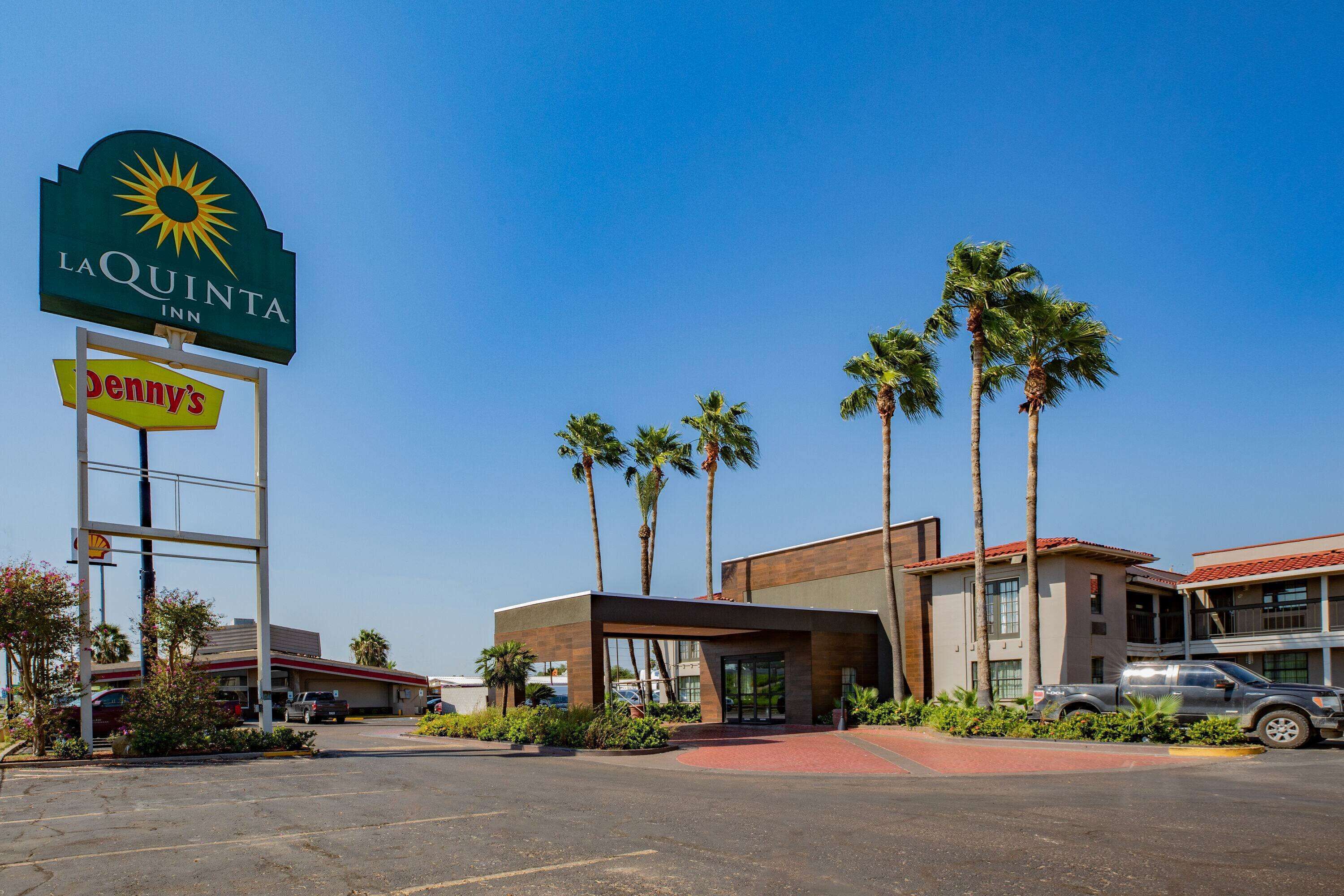 A La Quinta Inn with a 'Denny's' sign, palm trees, and a parking lot.
