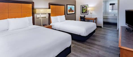 A hotel room with two beds, a desk, a chair, a TV, and a bathroom visible through an open door.