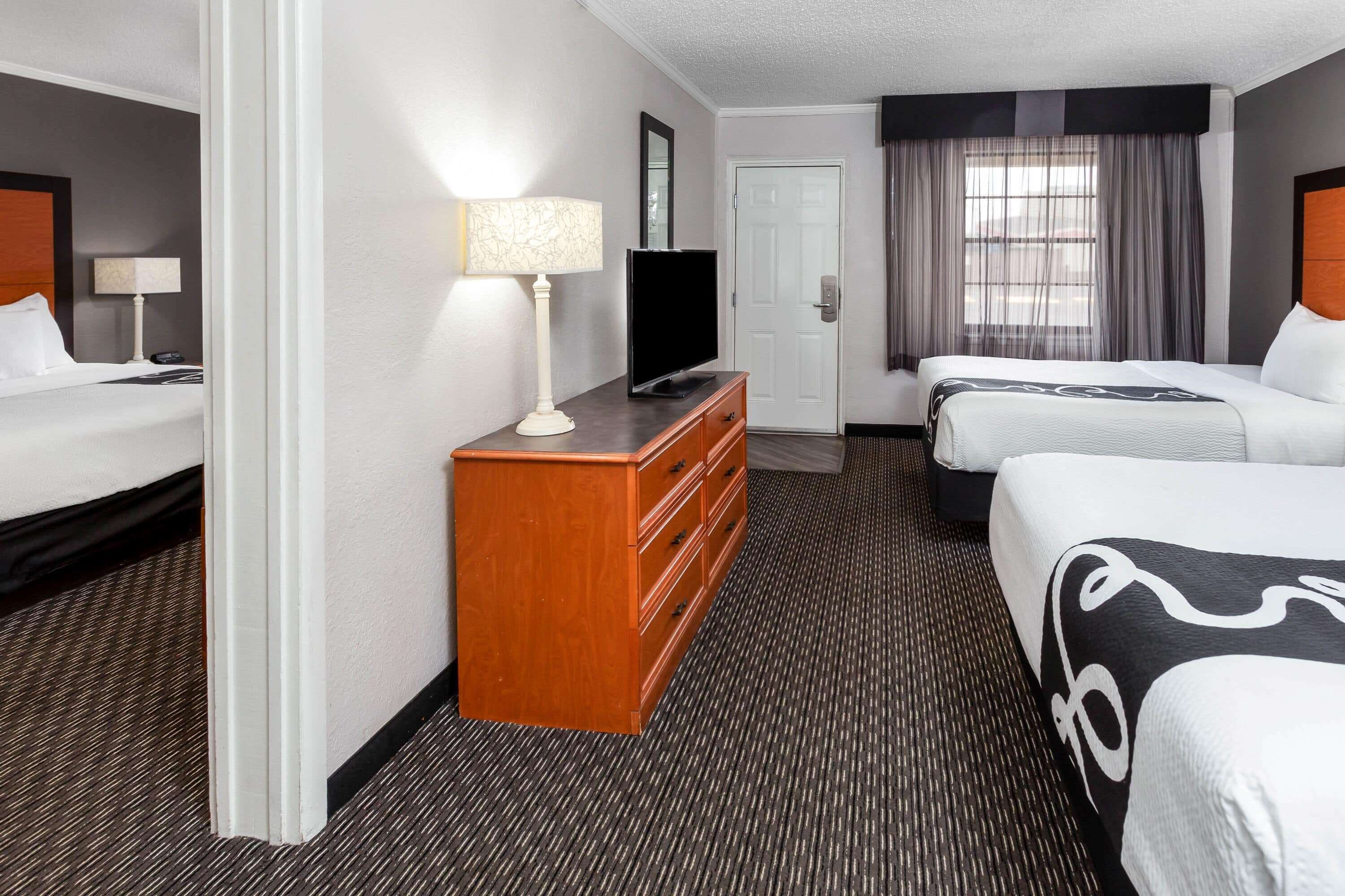 Ein Hotelzimmer mit zwei Betten, einem Fernseher, einem Schminktisch und einer Tür.