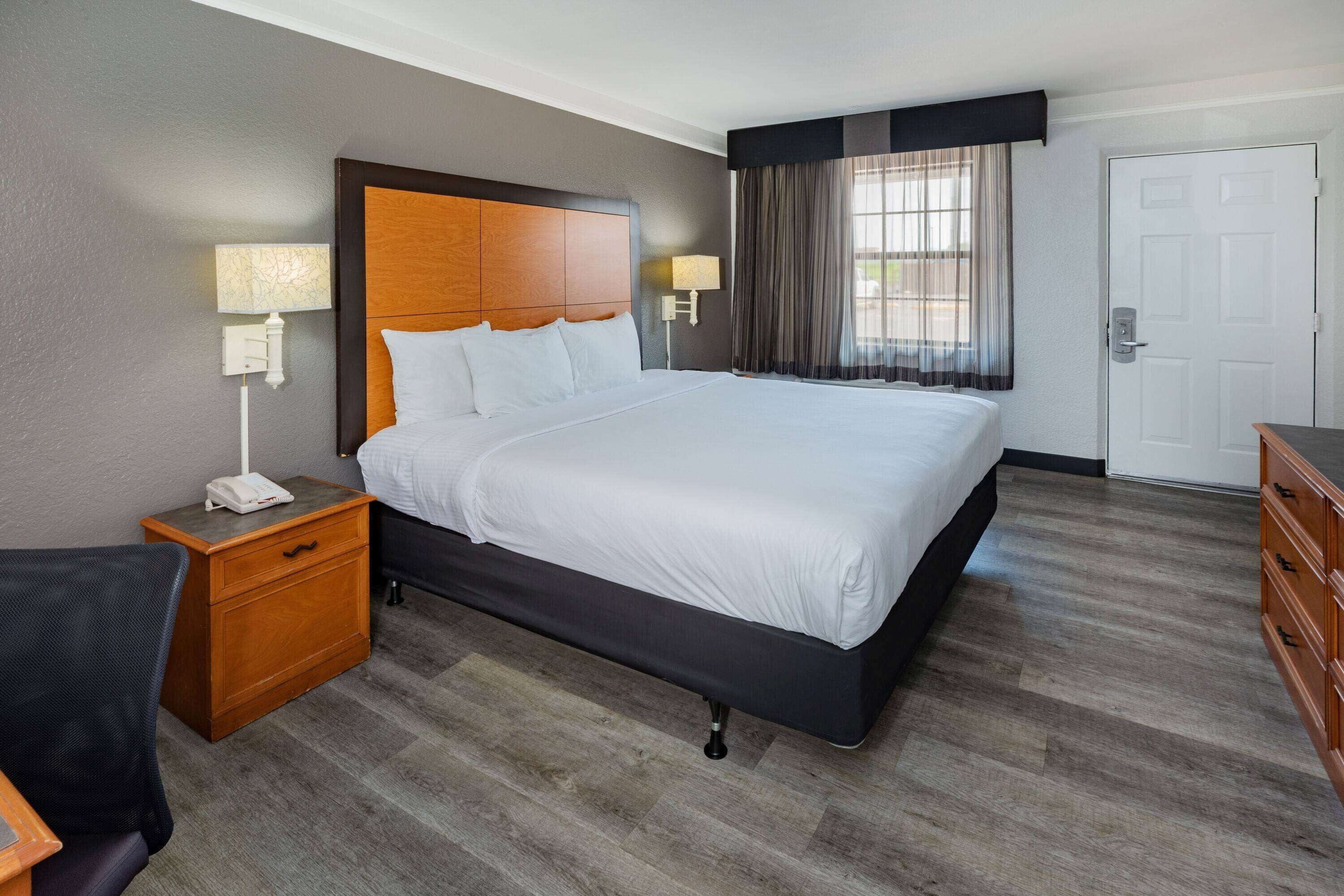 A hotel room with a large bed, wooden headboard, two bedside tables with lamps, a dresser, and a door.