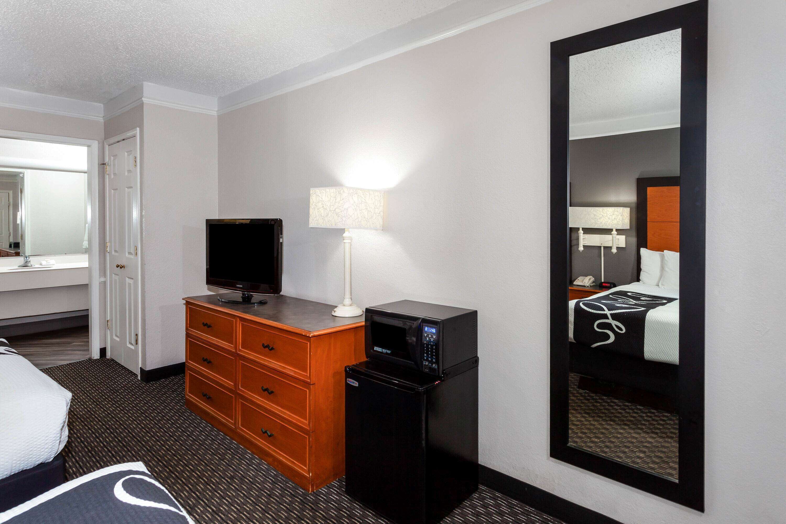 A hotel room with a bed, a television, a desk with a lamp, a microwave, and a large mirror.