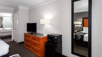 A hotel room with a bed, a television, a desk with a lamp, a microwave, and a large mirror.