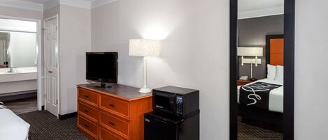 A hotel room with a bed, a television, a desk with a lamp, a microwave, and a large mirror.