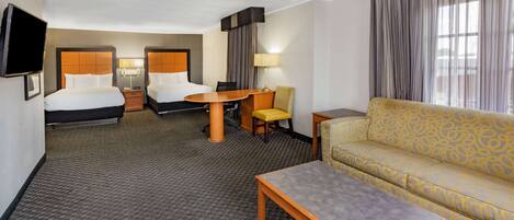 Een hotelkamer met twee bedden, een bank, een tafel, een televisie en een bureau.