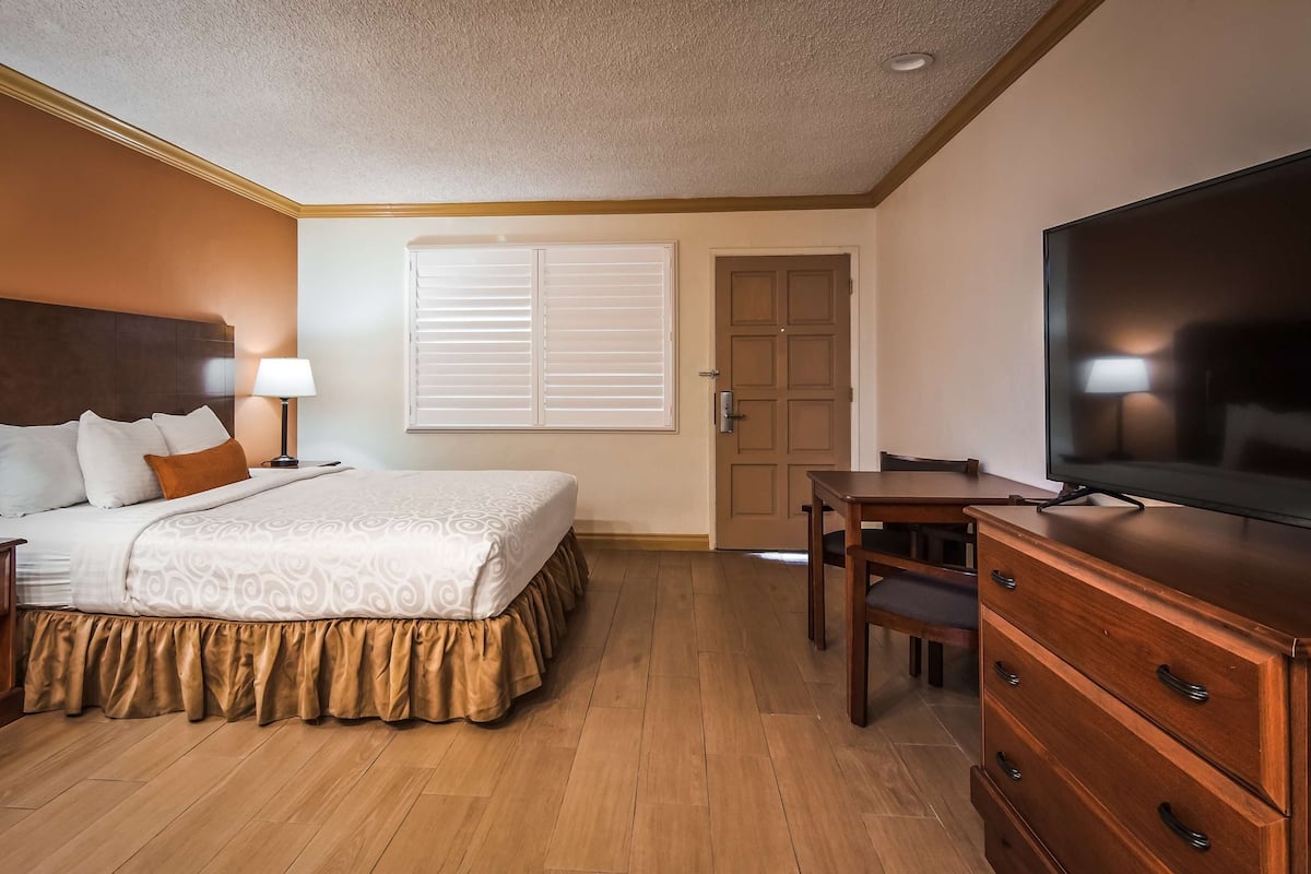 A hotel room with a bed, bedside tables, a TV, a desk, and a door.