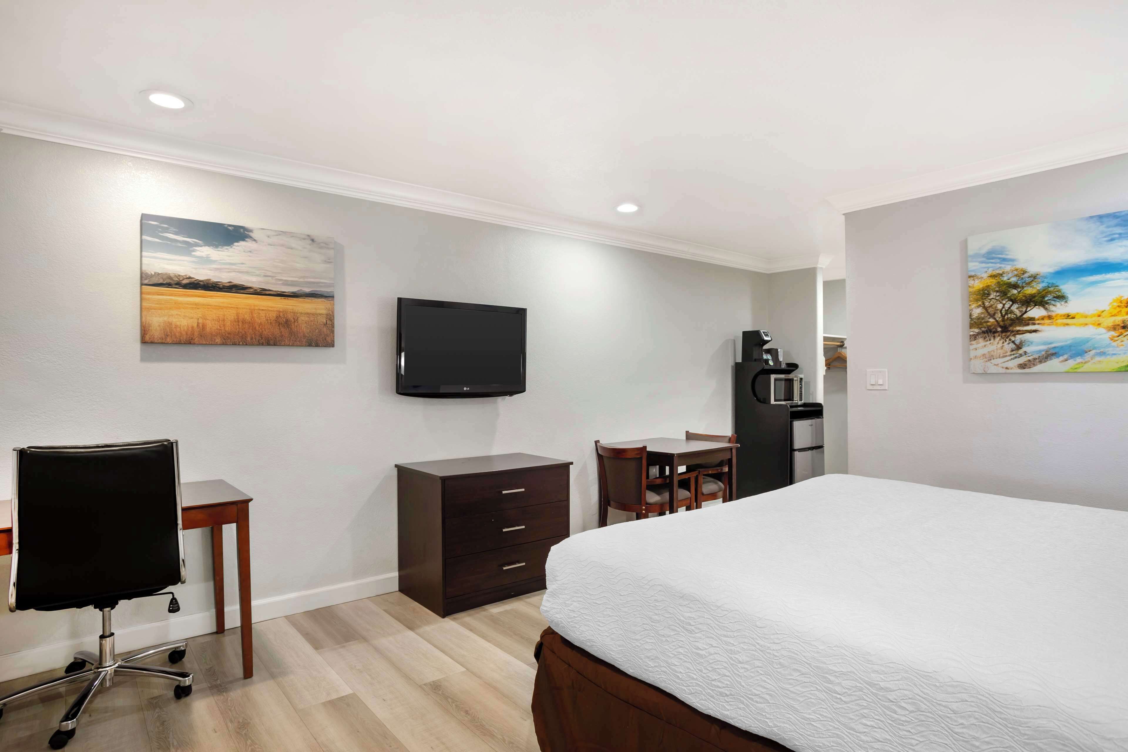 A hotel room with a bed, a desk, a chair, a television, and a small kitchenette.
