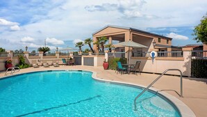 Ein Swimmingpool mit Liegestühlen und Sonnenschirmen, umgeben von einem Gebäude mit einer überdachten Terrasse.