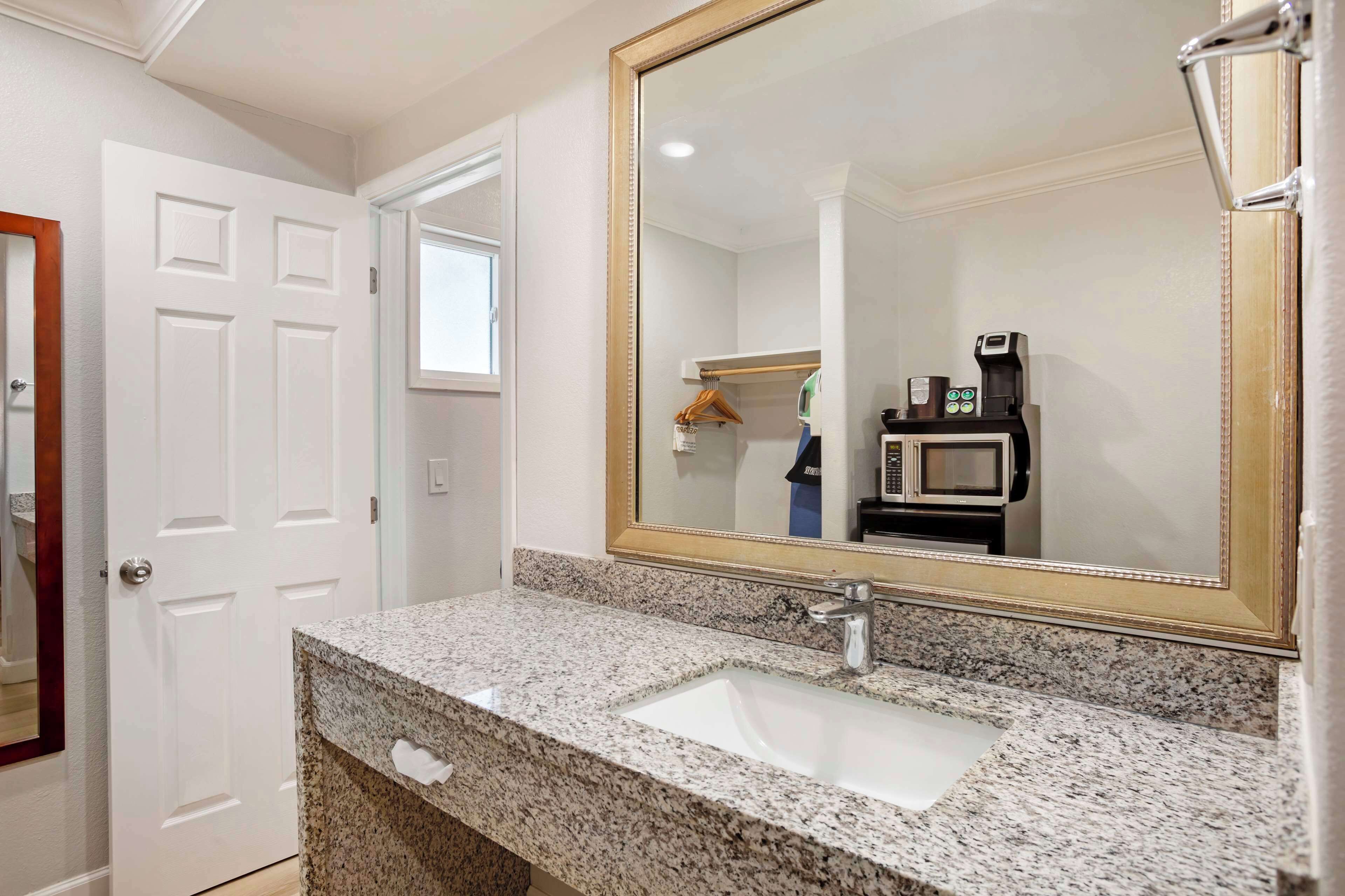 A bathroom with a granite countertop sink, a large mirror, and a coffee maker.