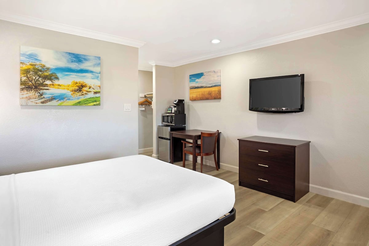 A hotel room with a bed, a desk with a chair, a television, and artwork on the walls.