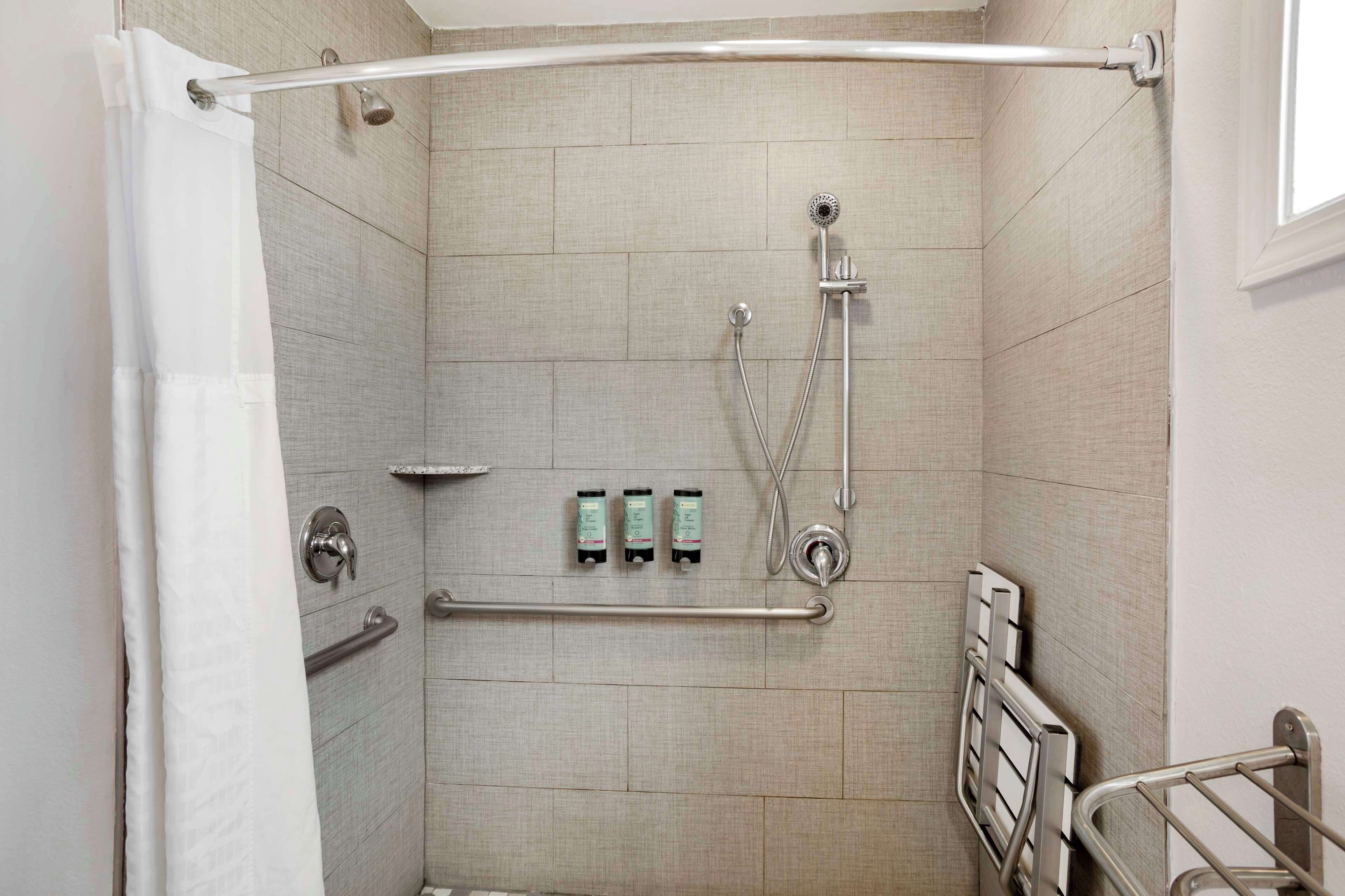 Une douche à l’italienne équipée d’une barre d’appui, d’un pommeau de douche et de trois bouteilles de shampoing.