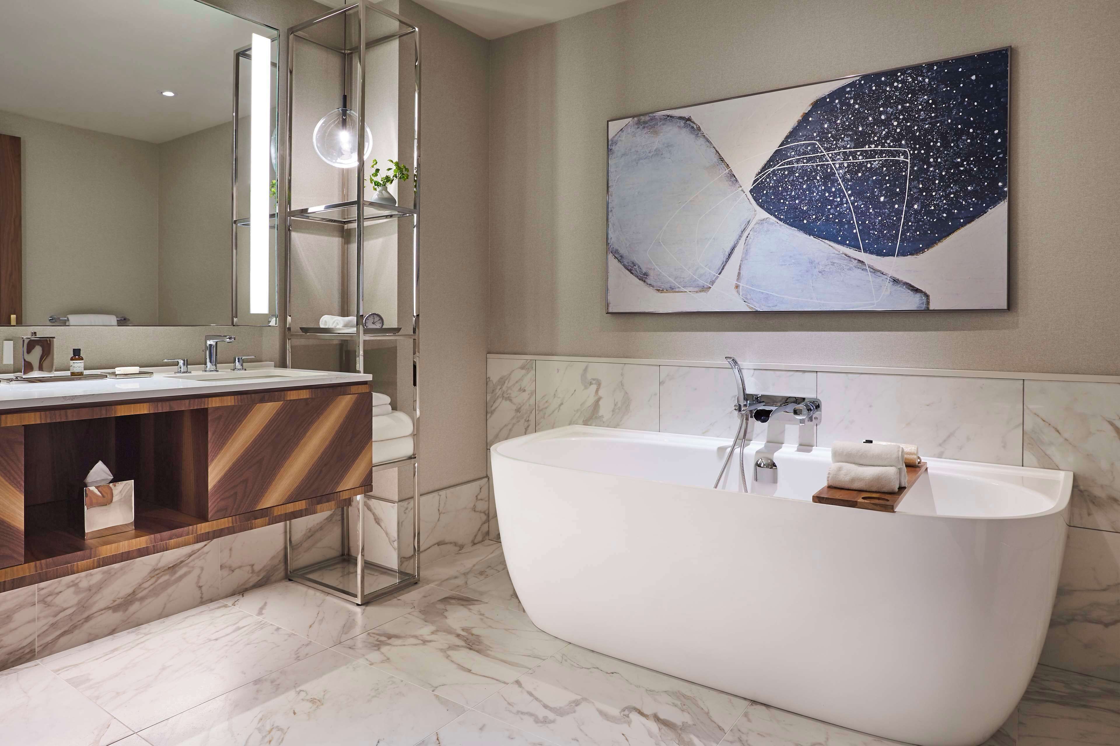 A modern bathroom with a freestanding bathtub, a vanity with a mirror, and a large abstract painting on the wall.